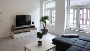 A modern living room with a flat-screen TV, a sofa, a coffee table, and two potted plants.