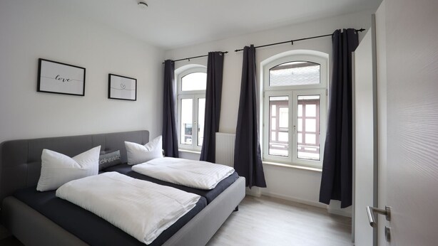 A bedroom with two beds, a window with curtains, and two framed pictures on the wall.