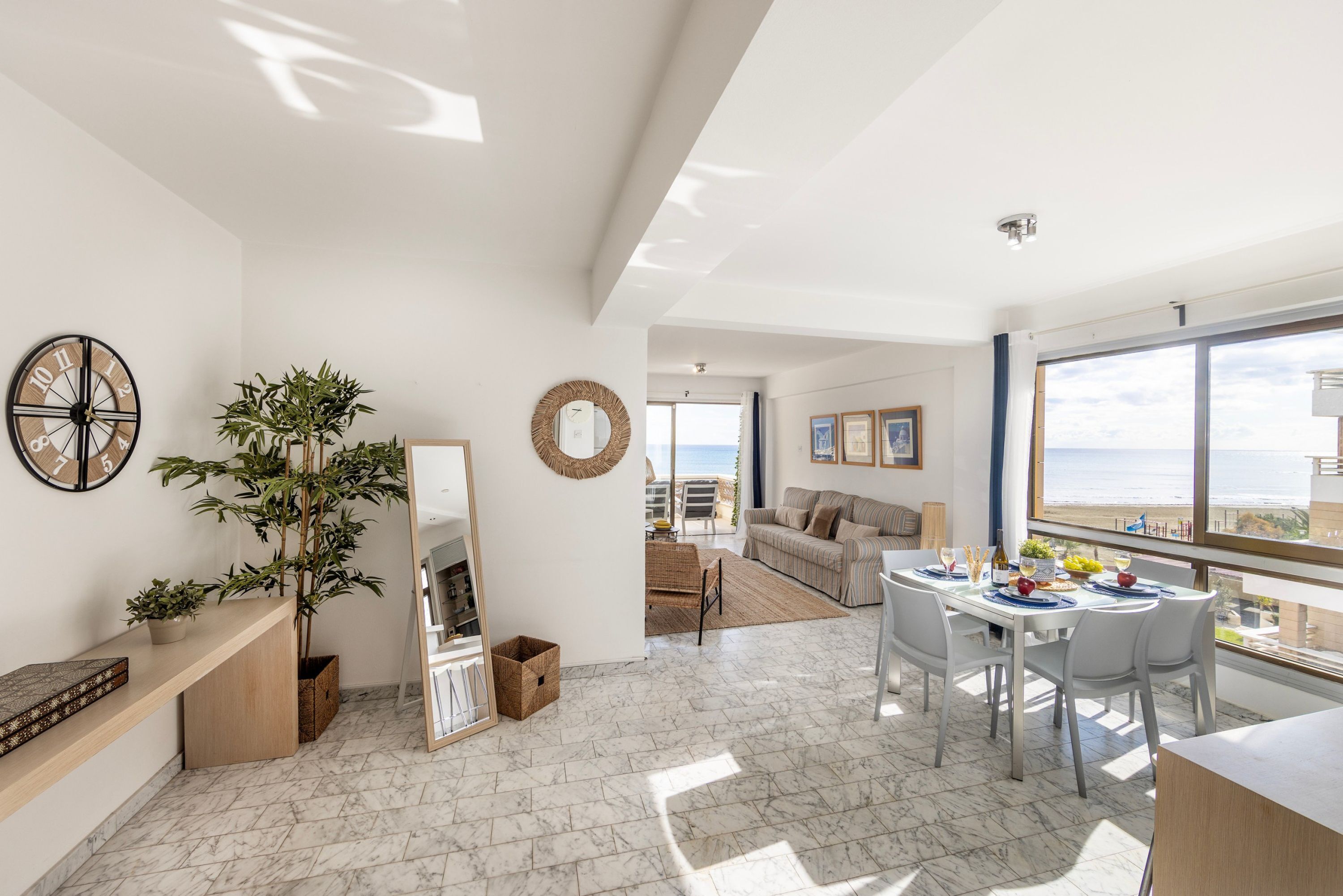 A spacious living area with a dining table set for four, a large mirror, and a potted plant.