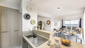 A modern kitchen with a sink, dining area with a table set for two, and a view of the sea.