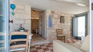 A room with a checkered floor, stone walls, a wooden chair, a sofa, and a door leading to another room. - Campanile Apartment With Terrace by Wonderful Italy (Ostuni)