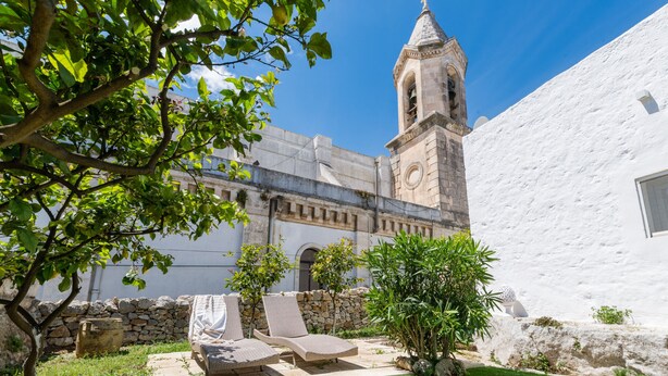 A courtyard with a stone wall, a white building, and a bell tower. - Campanile Apartment With Terrace by Wonderful Italy (Ostuni)