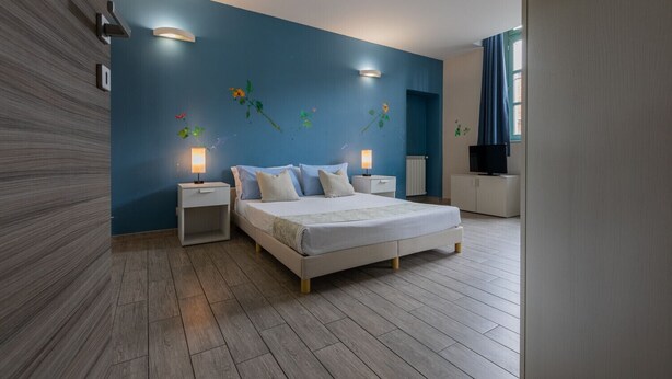 A modern bedroom with a large bed, two bedside tables, a TV, and decorative wall art. - Housing Giulia - Studio 2 4 by Wonderful Italy (Turin)