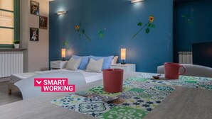 A modern bedroom with a blue accent wall, a bed with white bedding, two bedside tables with lamps, a coffee table with a colorful table runner, and a red mug. - Housing Giulia - Studio 2 4 by Wonderful Italy (Turin)