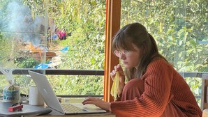 Iemand gebruikt een laptop aan een houten tafel, met een laptop tas en een mok erboven.