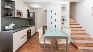 A modern kitchen with a dining area, featuring a glass table and white chairs, a microwave, and a coffee maker. - Aquamarine Terrace by Wonderful Italy (Syracuse)