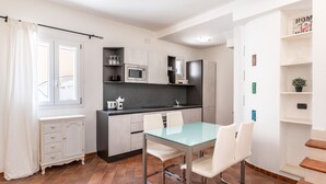 A compact kitchen with a dining area, featuring a glass table and white chairs, a microwave, and a small refrigerator. - Aquamarine Terrace by Wonderful Italy (Syracuse)