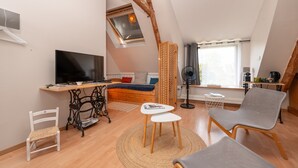 A loft-style room with a bed, a TV, a dining table, and a fan. - Embellie B&B – Guest Rooms with Shared Terrace, Garden & Wi-Fi (Baden)