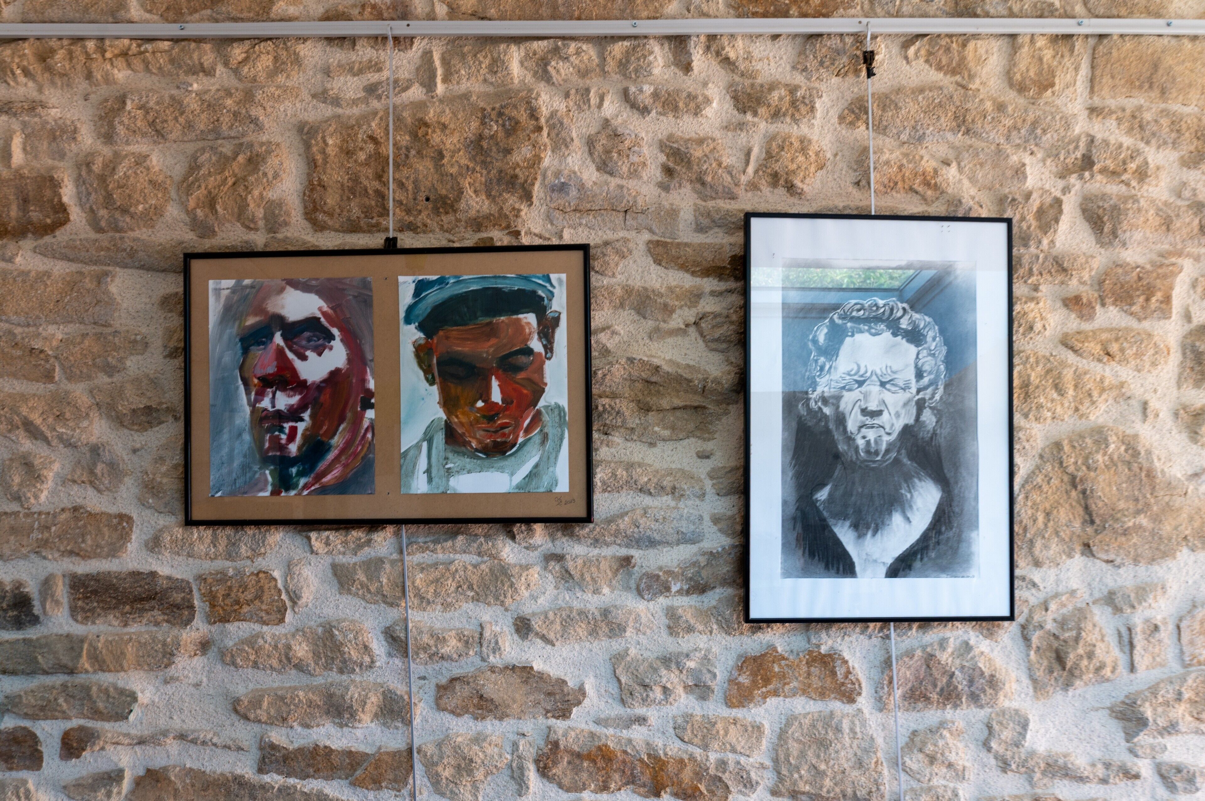 Deux œuvres d’art encadrées sont accrochées à un mur en pierre.