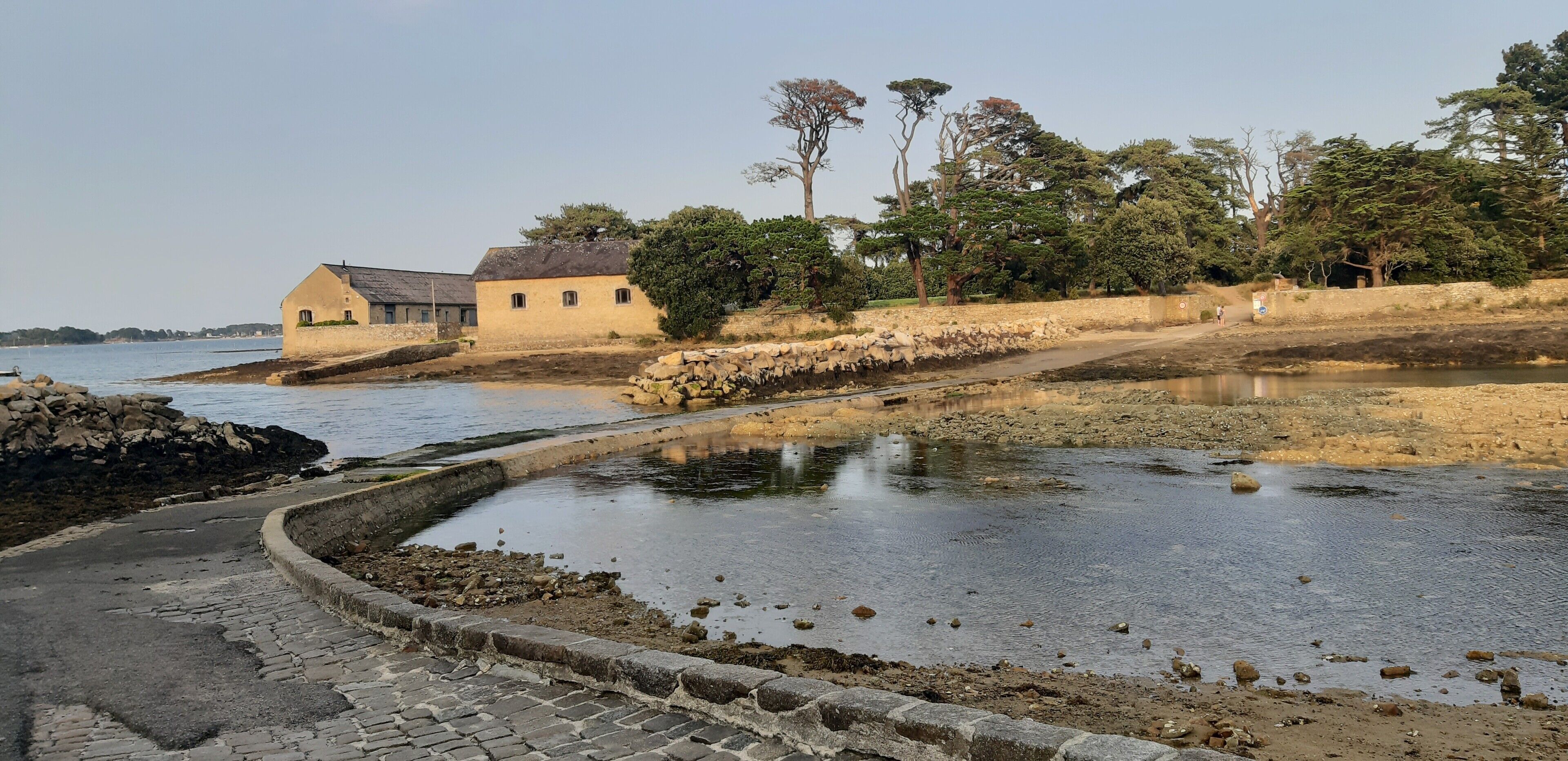 Un paysage côtier avec un sentier en pierre, un petit plan d’eau et un bâtiment doté d’un toit en pente.
