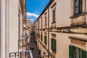 A narrow street with buildings on either side, featuring balconies and green shutters. - Casa Amalfitana by Wonderful Italy (Syracuse)