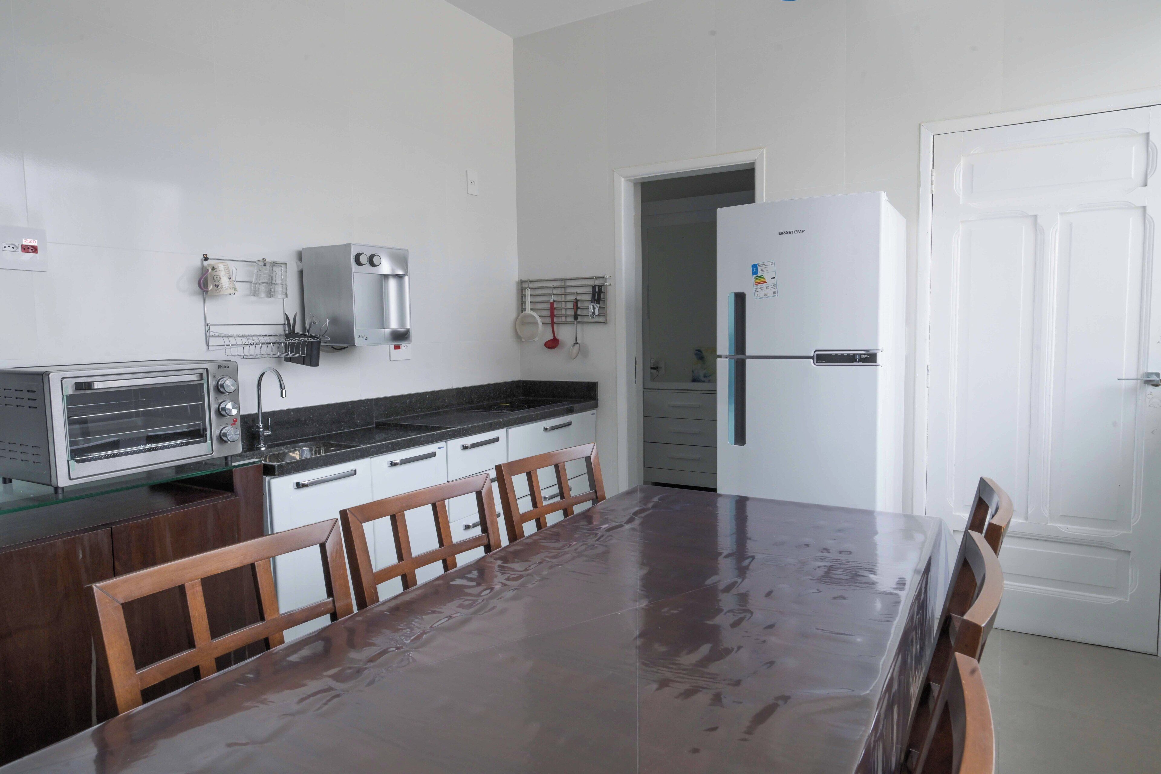 A kitchen with a stainless steel toaster, a white refrigerator, and a wooden dining table with chairs.