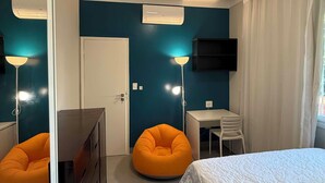 Een slaapkamer met een bed, een bureau, een stoel, een slaapzak, een dressoir, een airconditioner en een televisie.