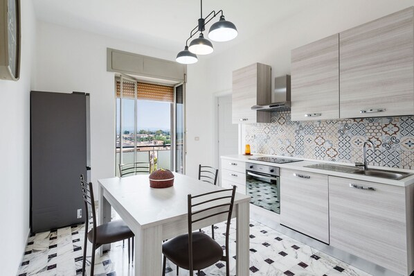 A modern kitchen with a dining area, featuring a large window, a built-in oven, and a patterned backsplash. - Casa Adda by Wonderful Italy - Urano (Syracuse)