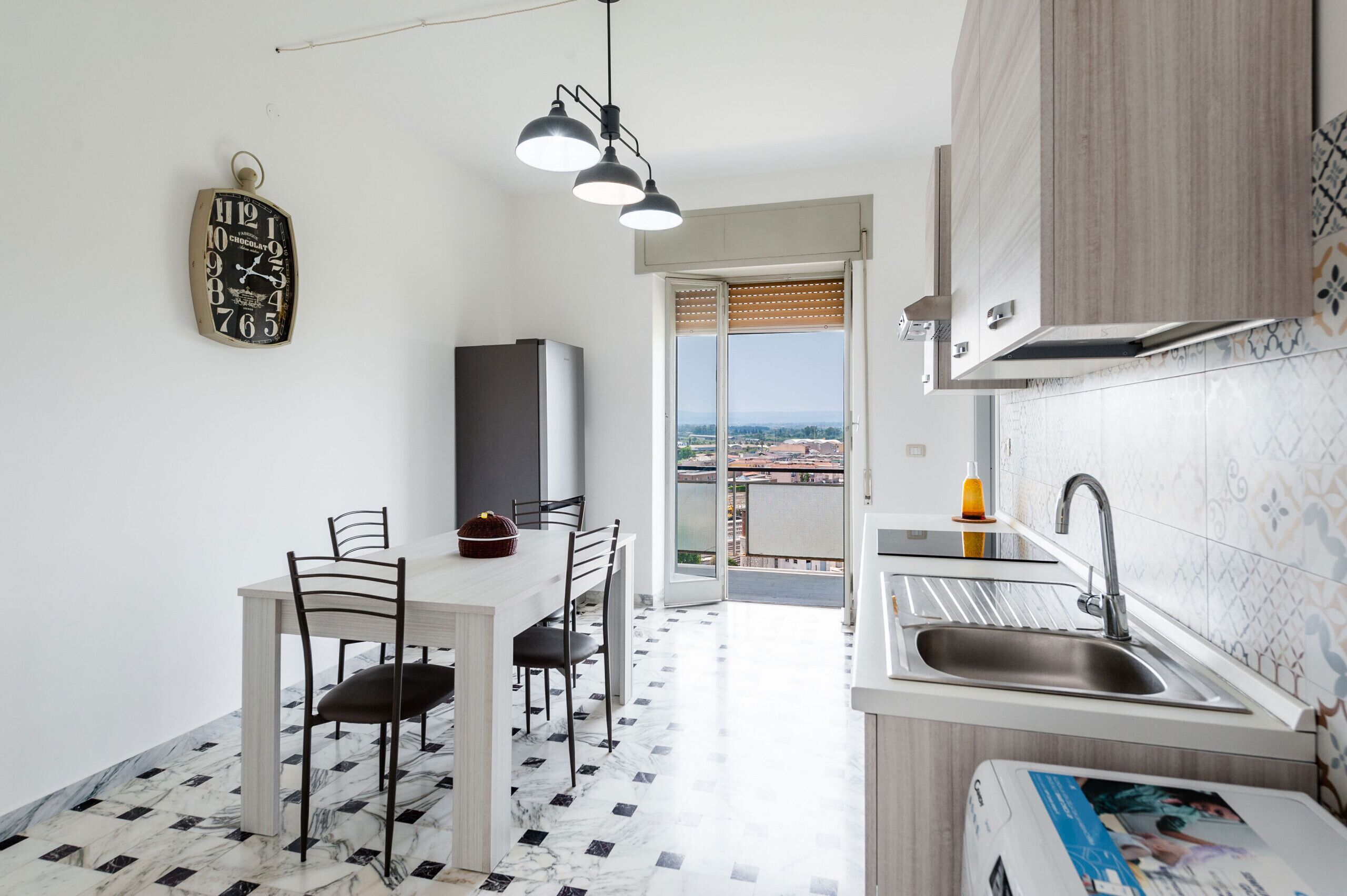 A modern kitchen with a dining area, a view through the door, and a clock on the wall.