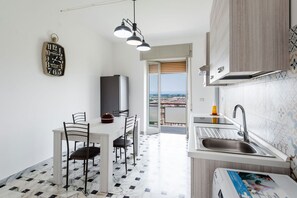 A modern kitchen with a dining area, a view through the door, and a clock on the wall. - Casa Adda by Wonderful Italy - Urano (Syracuse)
