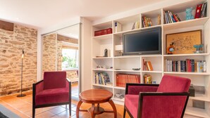 A living room with a stone wall, a large flat-screen TV, and two red chairs. - Voyage B&B with Shared Terrace, Communal Garden & Wi-Fi (Baden)