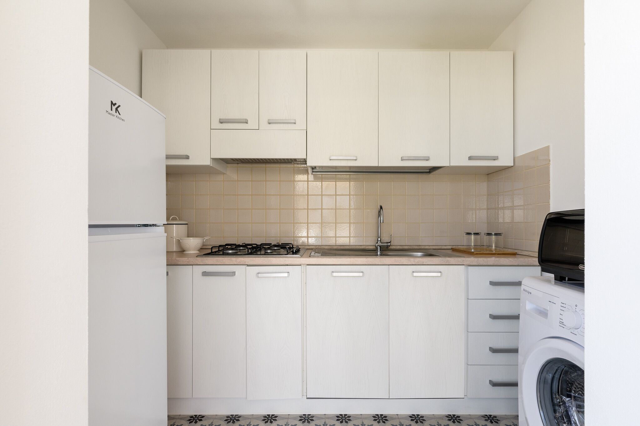 A compact kitchen with white cabinets, a stove, and a washing machine.
