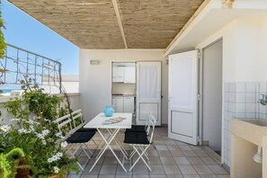 Een balkon met een tafel en stoelen, een kitchenette en een deur naar een badkamer.