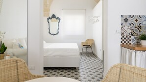 Ein Schlafzimmer mit einem Bett, einem Sessel, einem kleinen Tisch und einem dekorativen Spiegel.