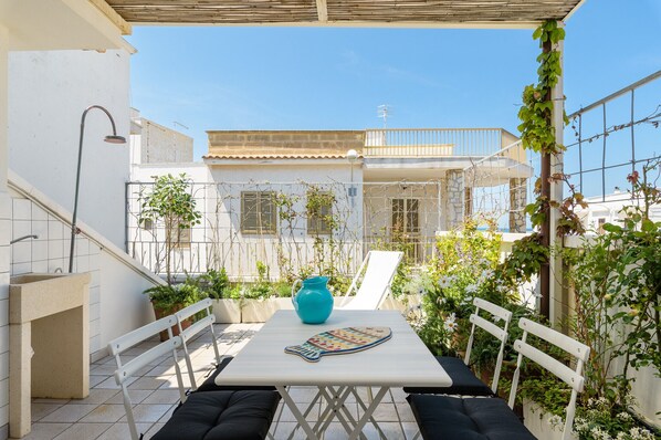 Een terras met een tafel, stoelen, een blauwe kruik en een betegelde muur.