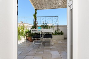 Een terras met twee witte stoelen en een tafel, een pergola en bloempotten.