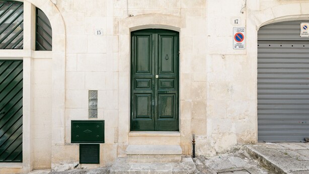 Un edificio con puerta verde, un portón de garaje cerrado y un cartel de no estacionamiento.