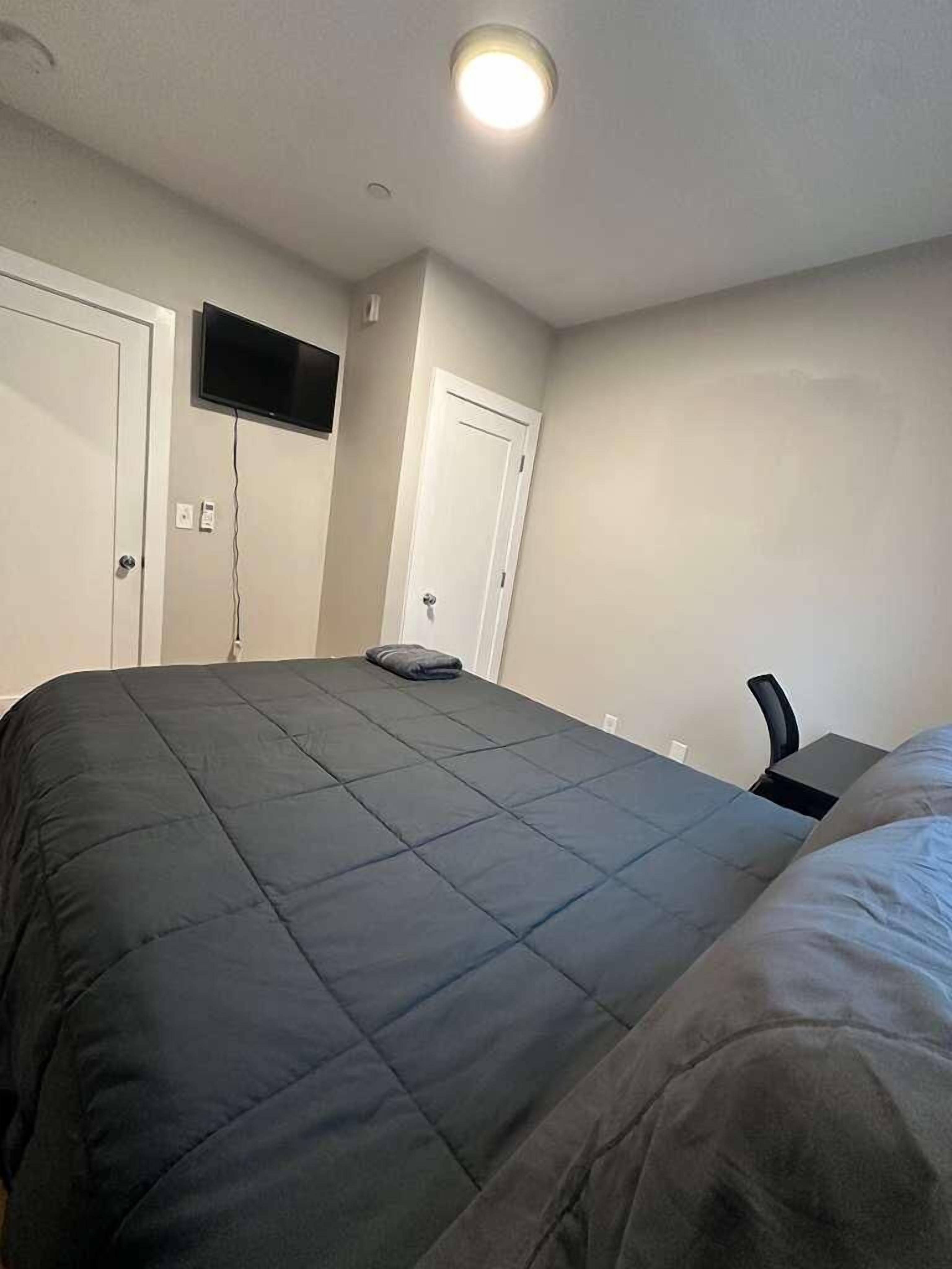 Een slaapkamer met een bed, een bureau en een televisie aan de muur.
