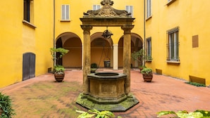 A courtyard with a central fountain, surrounded by yellow walls and potted plants. - Casa Ambrosini - Artemide Apt by Wonderful Italy (Bologna)