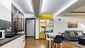 A modern kitchen with a microwave, sink, and wooden cabinets. There is a dining area with a table and chairs, and a gray sofa with a throw pillow. - Casa Ambrosini - Artemide Apt by Wonderful Italy (Bologna)