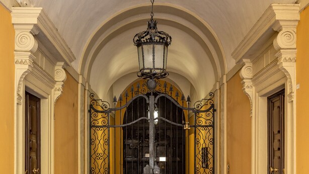 A hallway with a polished floor, a decorative iron gate, and a hanging light fixture. - Casa Ambrosini - Artemide Apt by Wonderful Italy (Bologna)