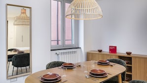 Een moderne eetruimte met een houten tafel voor vier personen, een grote spiegel en een hanglamp.