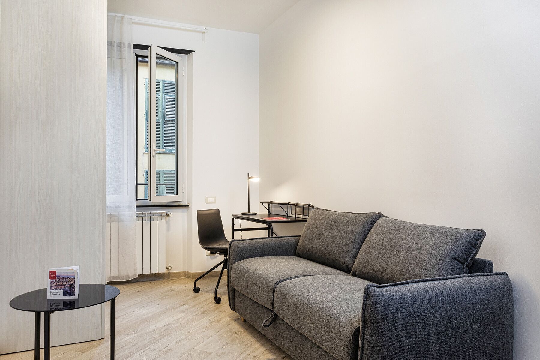 Una habitación pequeña y moderna con un sofá gris, una mesita y un escritorio con lámpara.