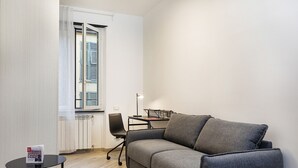 Egy kis, modern szoba, melyben szürke kanapé, egy kis asztal és egy lámpával felszerelt íróasztal található.