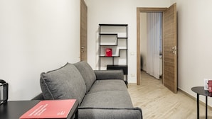 Egy modern nappali, szürke kanapéval, egy kis fekete asztallal és egy piros könyvvel. A szobában egy fa könyvespolc található, melynek középső polcán egy piros könyv áll. A szoba falai fehérre vannak festve, a padló pedig fából készült.