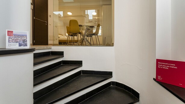 A staircase leading to a room with a glass door, a dining area with chairs and a table, and a red sign on the wall. - Il Veliero Loft by Wonderful Italy (Genoa)