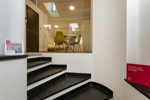 A staircase leading to a room with a glass wall, a dining area with chairs, and a red sign on the wall. - Il Veliero Loft by Wonderful Italy (Genoa)