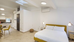 A modern hotel room with a large bed, a small table, and a chair. There is a kitchen area visible in the background. - Il Veliero Loft by Wonderful Italy (Genoa)