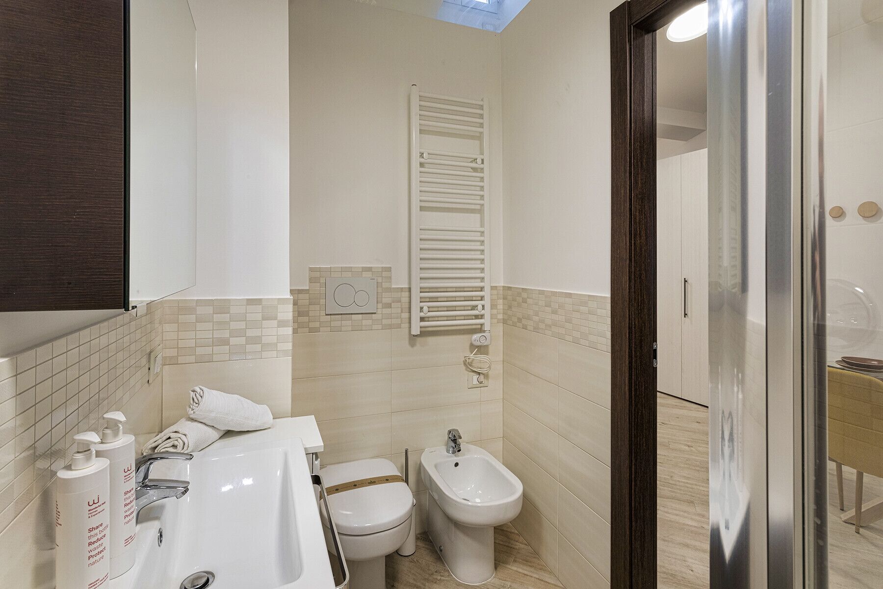 A bathroom with a white sink, toilet, and bidet, a towel rack, and a mirror.