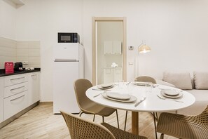 A modern kitchen with a microwave, refrigerator, and a dining area with a round table and wicker chairs. - Caravella Apartment by Wonderful Italy (Genoa)