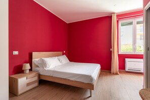 A bedroom with a bed, nightstand, lamp, and window with curtains. - 5 Colors by Wonderful Italy (Syracuse)