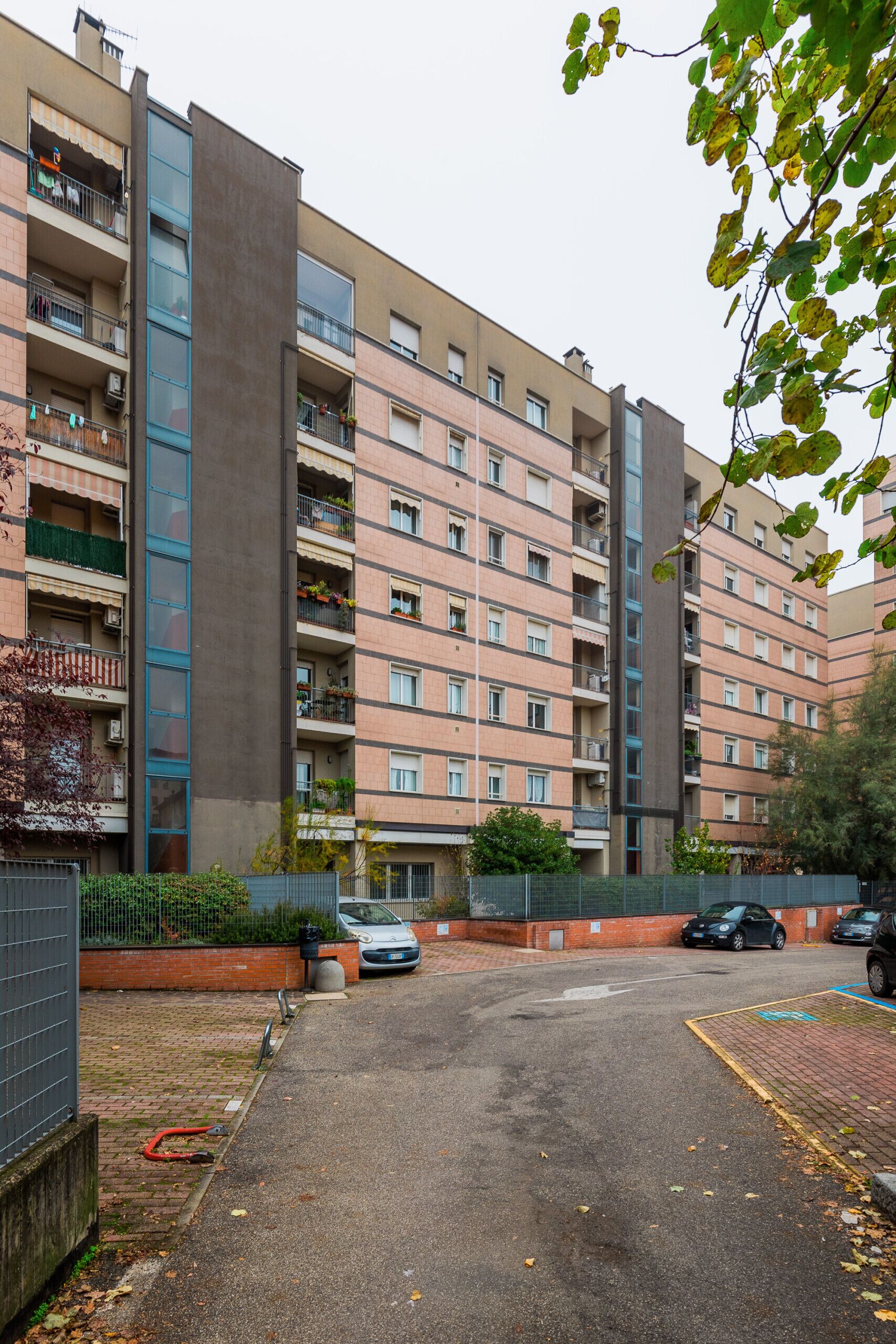 Un immeuble résidentiel à plusieurs étages, doté de balcons, d’un espace de stationnement et d’une entrée sécurisée par un portail.