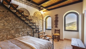 A bedroom with a stone wall, wooden staircase, and a view of the countryside through arched windows. - Traditional Ligurian House (Sanremo)