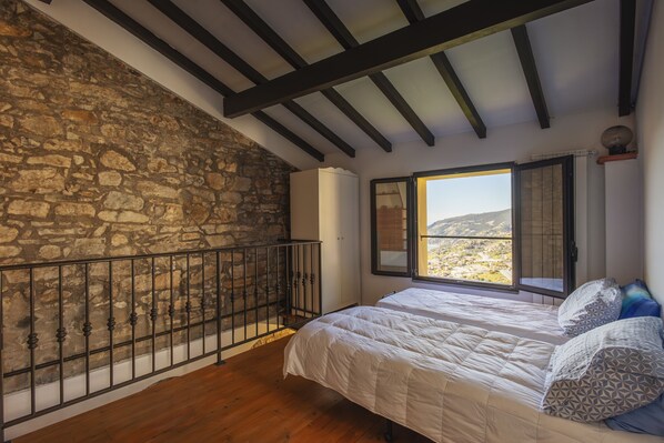 A bedroom with a stone wall, wooden floor, a bed with patterned pillows, and a window with a view. - Traditional Ligurian House by Wonderful Italy (Sanremo)