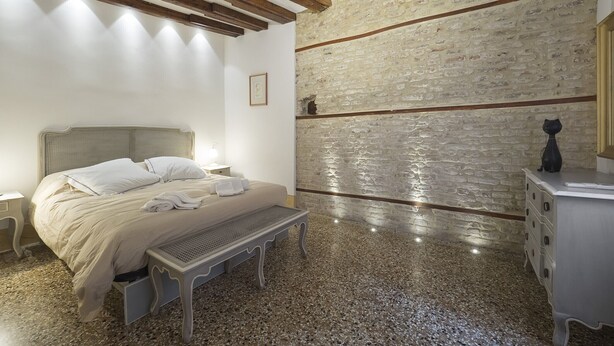 Une chambre à coucher avec un lit, un banc, une commode et un mur en pierre.