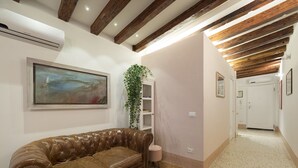 Un couloir avec un canapé en cuir marron, un tableau, une plante et une porte donnant sur une autre pièce.