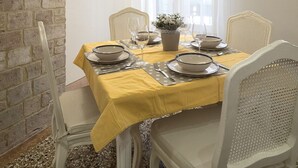 Un coin repas avec un mur en briques, des poutres en bois, une nappe jaune, des chaises blanches et un luminaire suspendu.