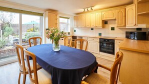 A kitchen with wooden cabinets, a dining table with a dark tablecloth, and a vase with flowers. - Host & Stay | Riders Rest (Wootton)