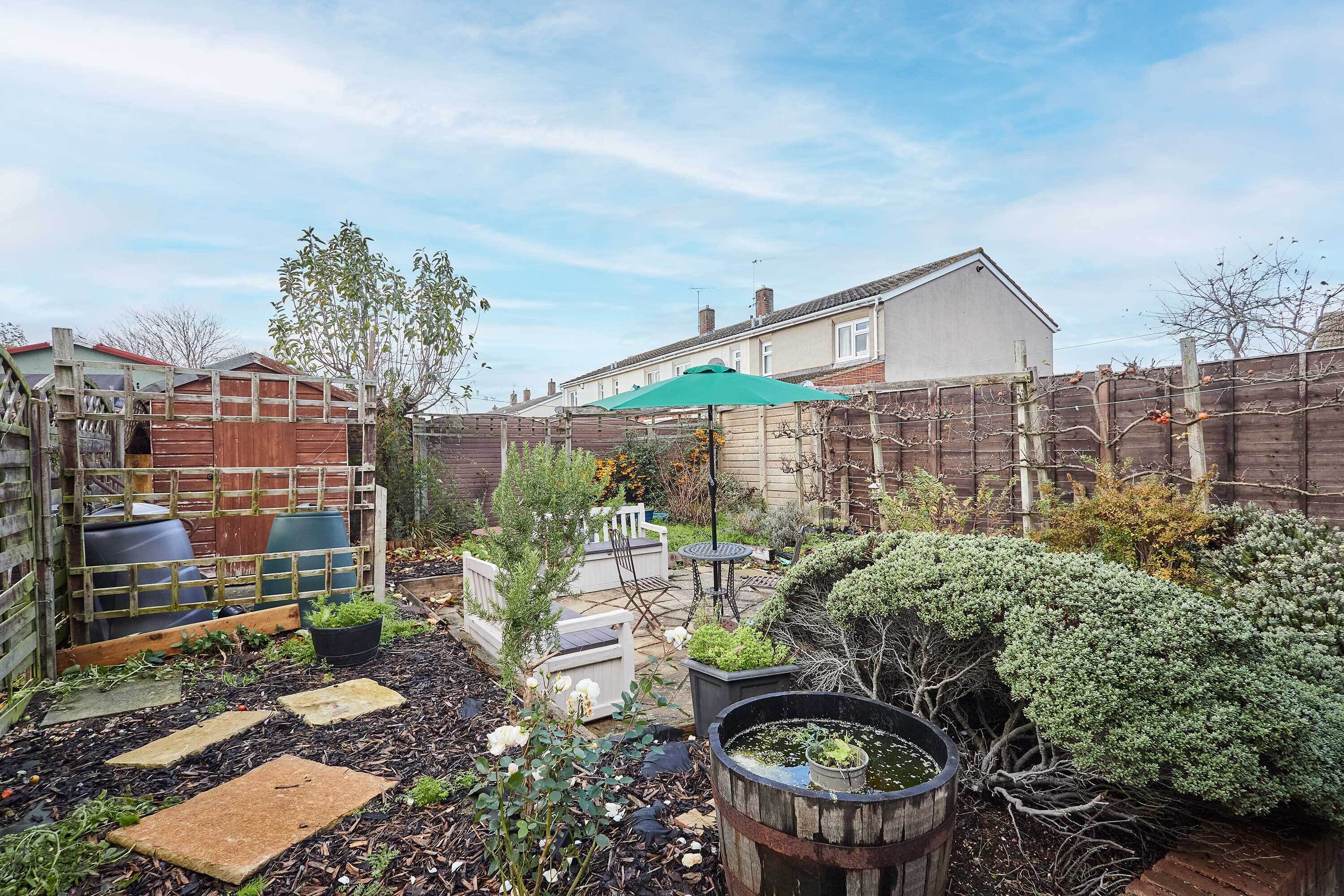 Un jardin avec une clôture en bois, une chaise blanche, une table et un parasol vert.