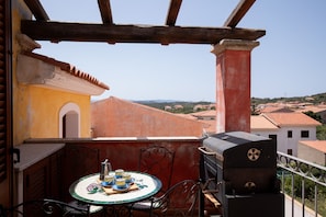 Een balkon met een tafel gedekt voor thee, een barbecue en uitzicht op de omliggende gebouwen.